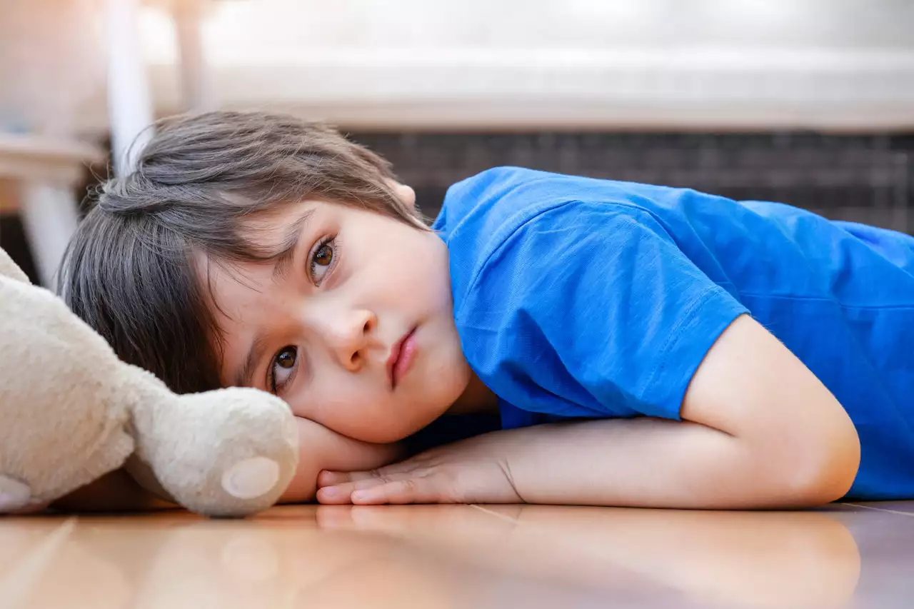 Ein Junge liegt mit seinem Stofftier traurig auf dem Boden.