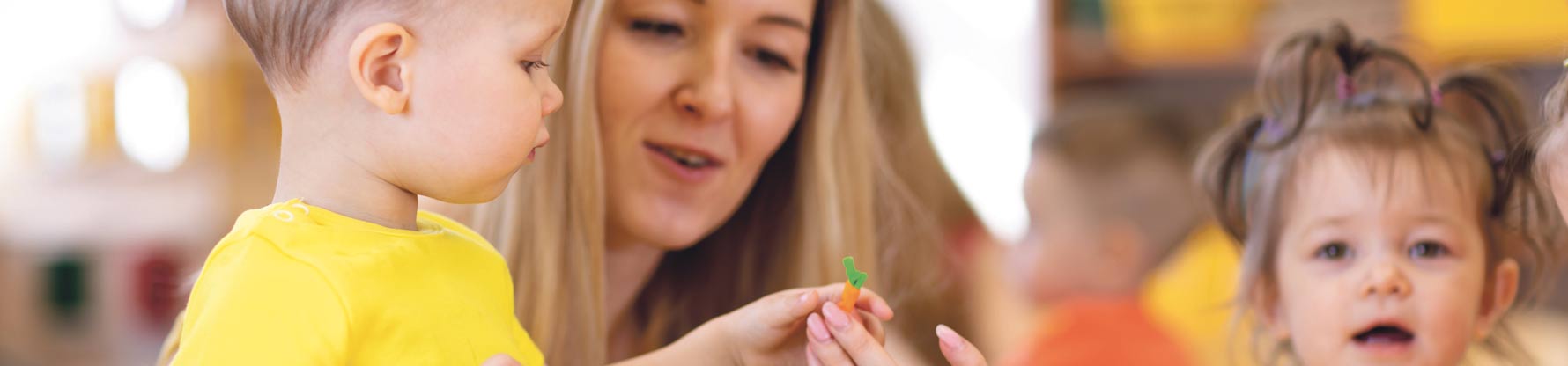 Eine Erzieherin zeigt einem kleinen Jungen eine Spielzeug-Möhre.