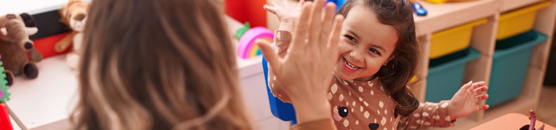 Eine Kindergarten-Mädchen klatscht sich mit ihrer Erzieherin ab.