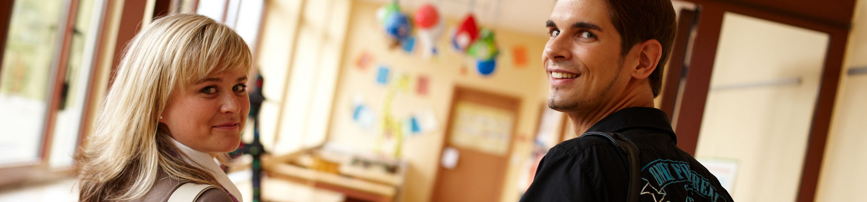 Eine junge Frau und ein junger Mann drehen sich beim Gehen um und schauen in die Kamera.