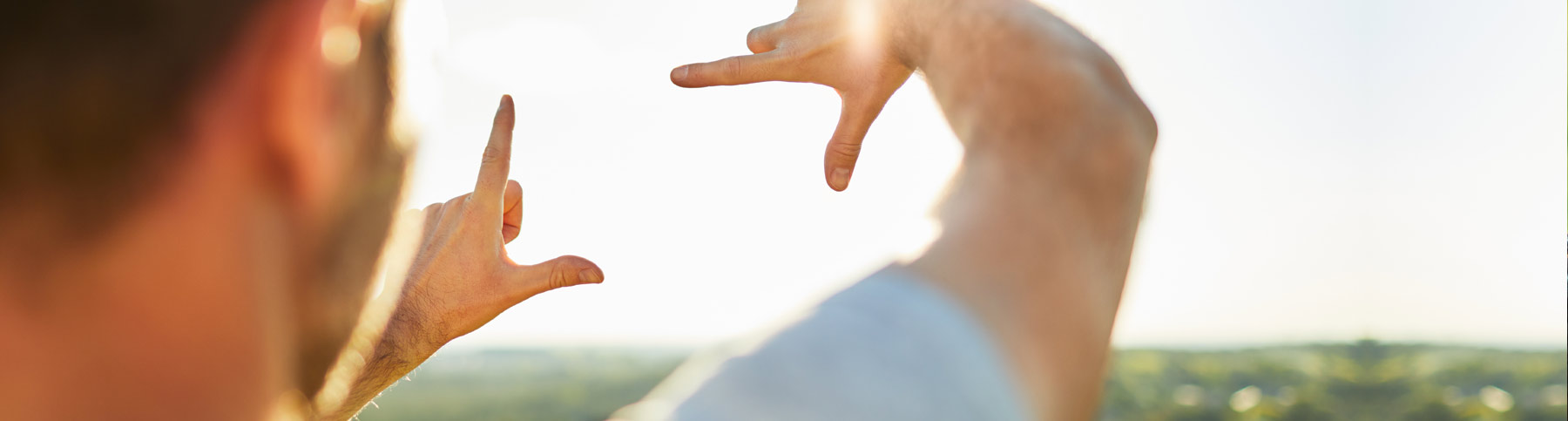 Ein Mann umrahmt mit den Händen die Sonne am Horizont.